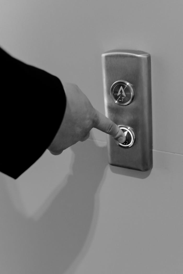 Monochrome image of a hand pressing an elevator button, focusing on detail and texture.